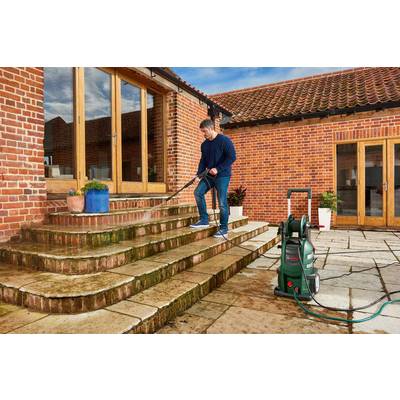 A person is cleaning a multi-level stone staircase with a pressure washer in front of a red brick house.