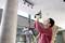 A man is standing on a ladder and drilling a hole in the ceiling to install a light fitting. Safety glasses and a screwdriver are visible.