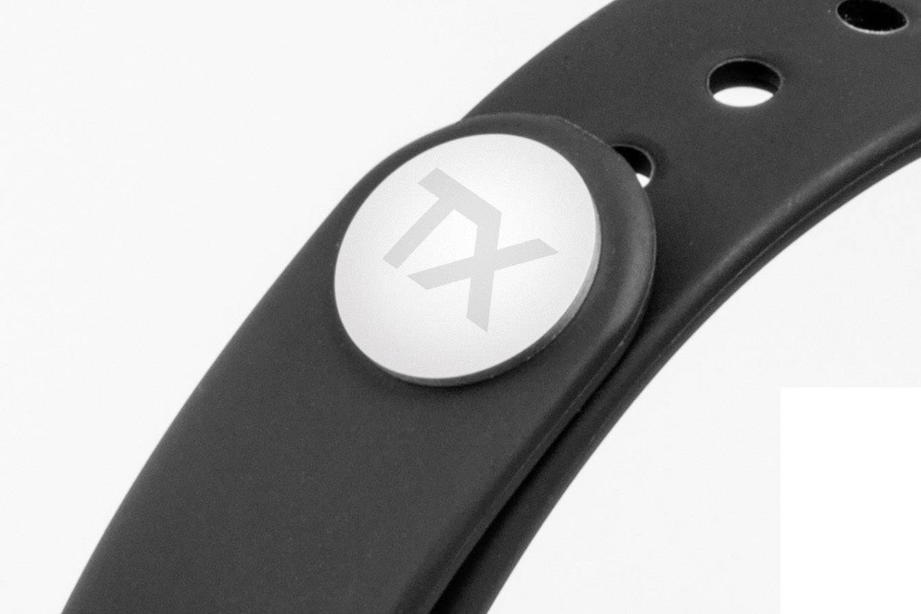 Black wristband with a round, silver-coloured button featuring 'TX' printed on it. The wristband has multiple holes for size adjustment.