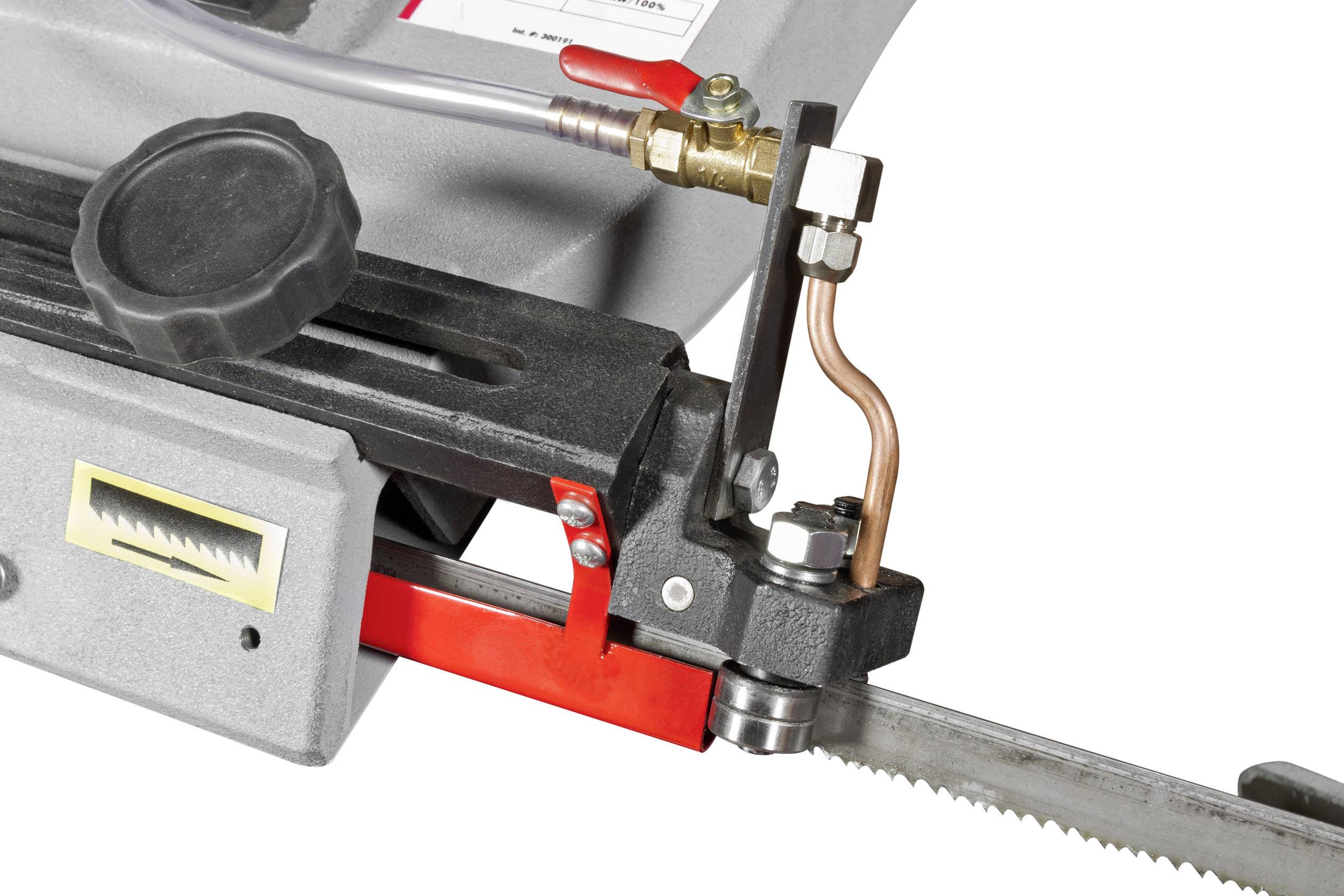 Close-up of a machine component with a saw blade. Visible are a black rotary knob, a copper pipe, and a scale.