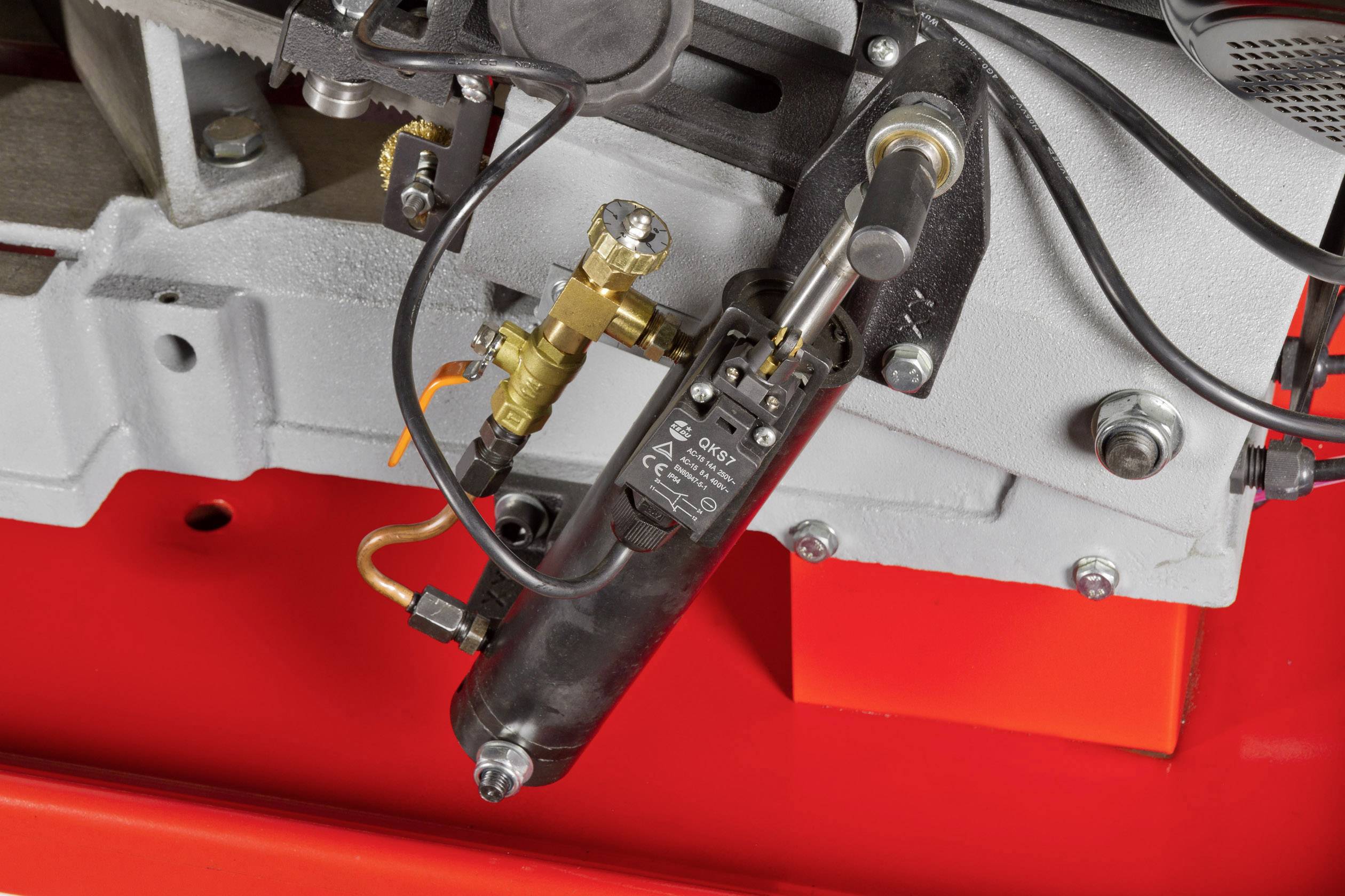 Close-up of a machine component with multiple connections and cables, including a black cylinder with valves and labels.