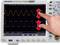A oscilloscope shows two waveforms. A hand points to a section of the waves to mark differences in height or amplitude.
