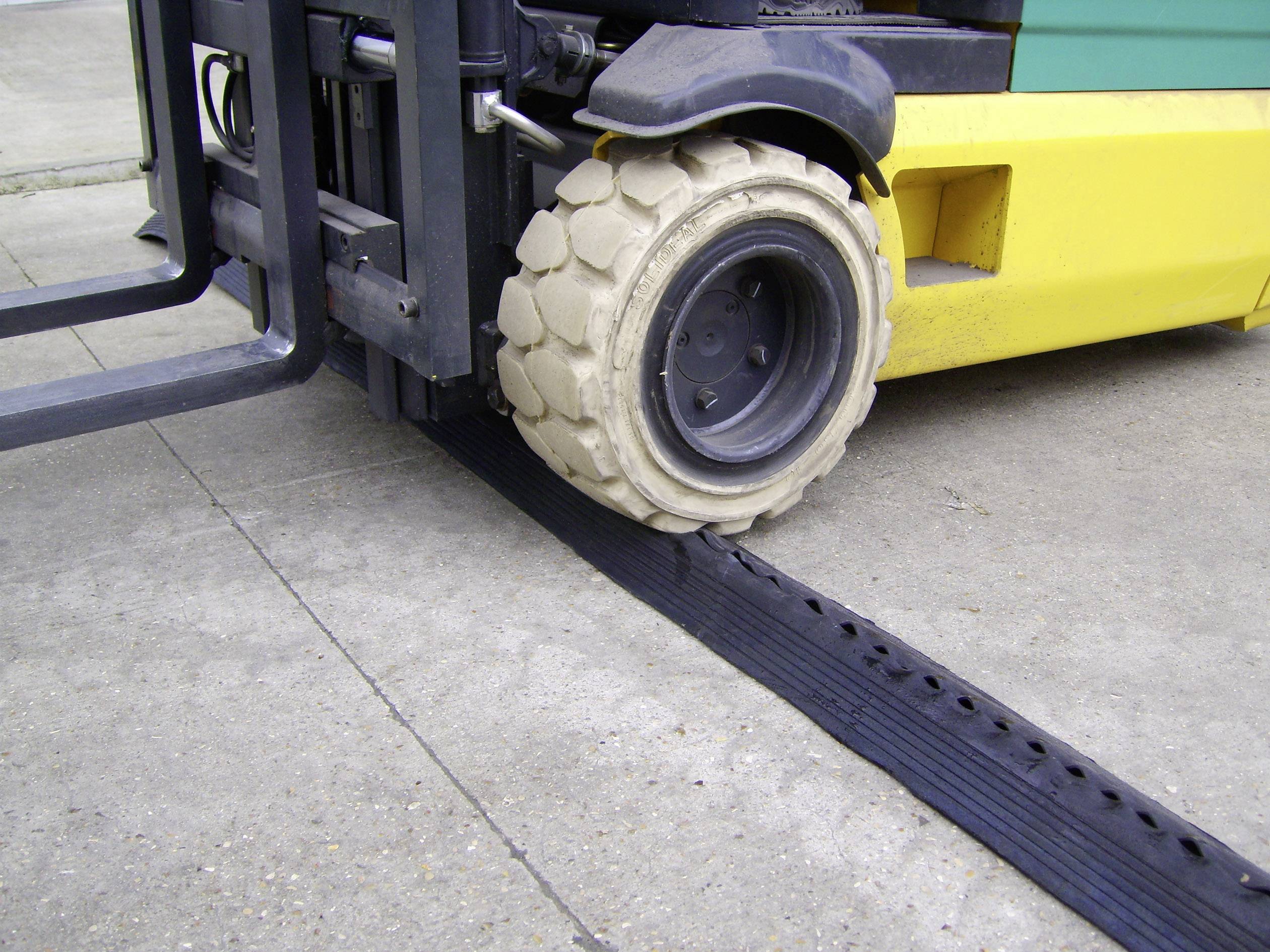 A forklift is driving over a rubber cable ramp, protecting cables on the ground.