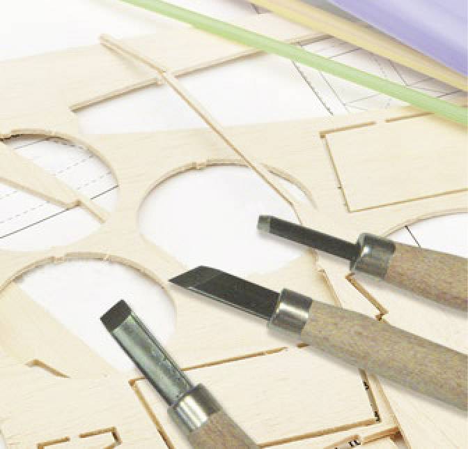 Three carving tools lie on wooden boards with cut-out shapes and a blueprint that is partially obscured.