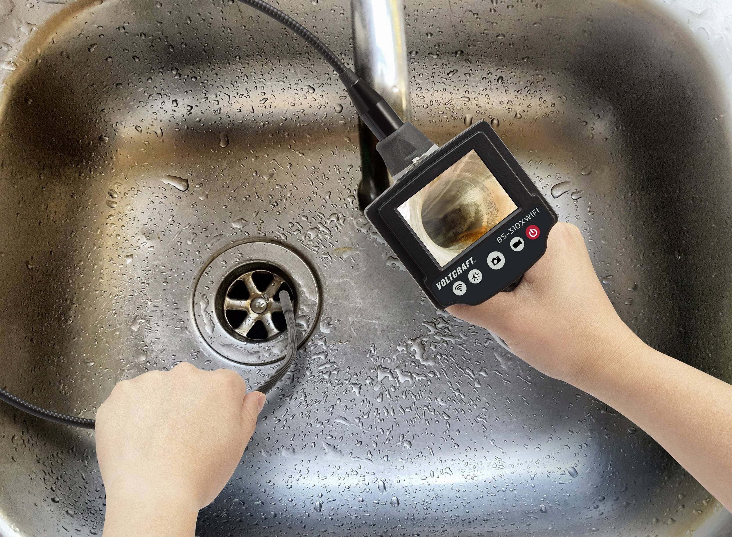 A person is holding an endoscope over a wet sink and examining the drain on the device's display.