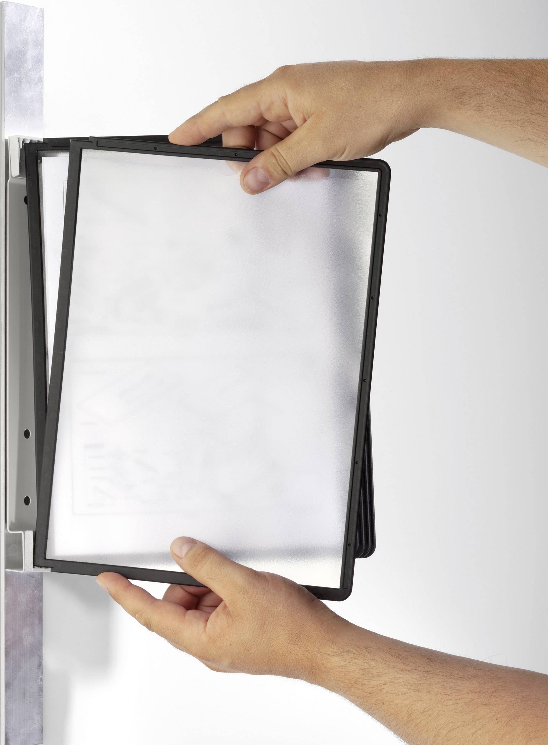 Hands securing a black frame or screen to a wall mounting.