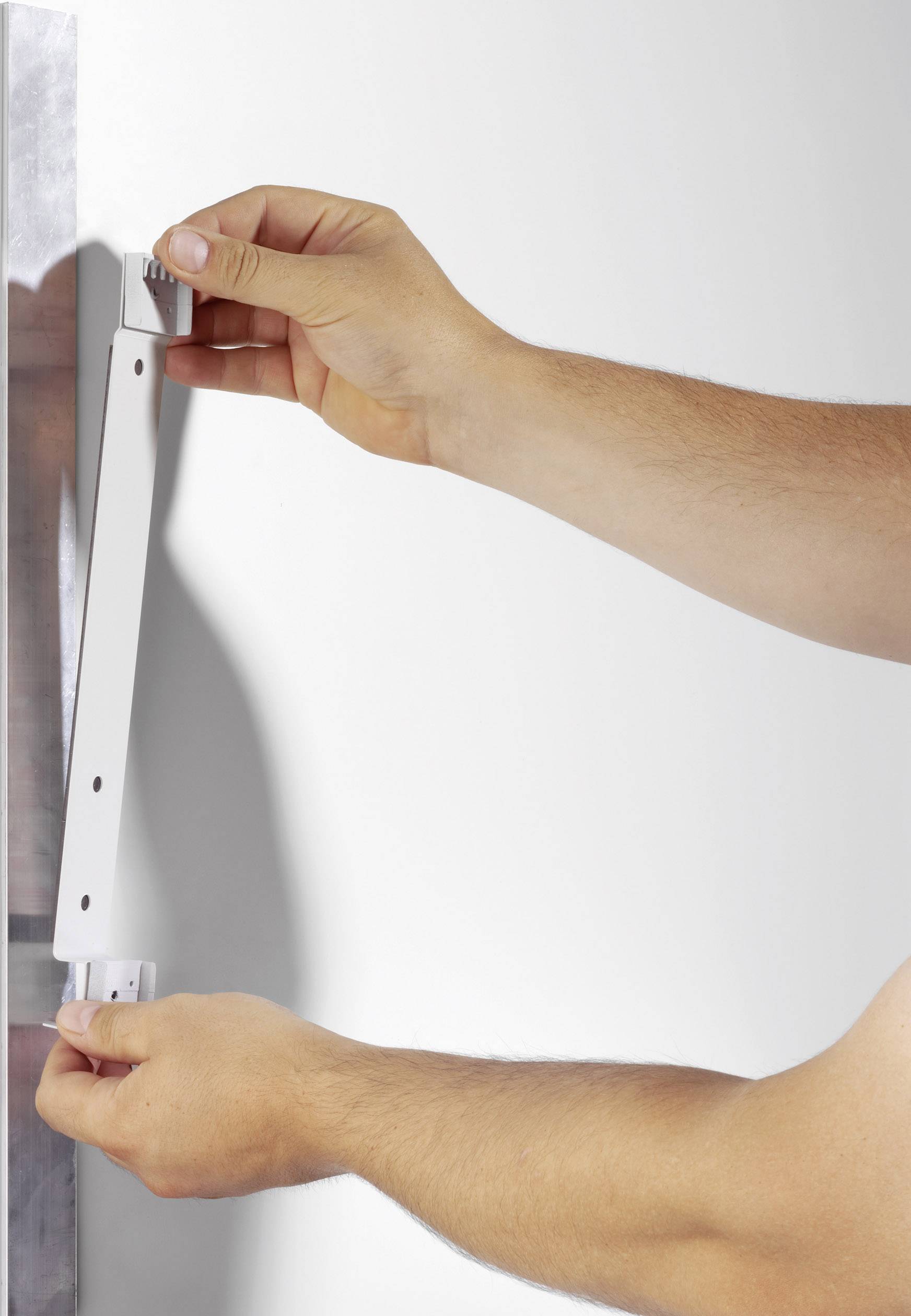 A person is attaching a white metal angle bracket to a wall. Their hands are holding the bracket at both ends to adjust its position.