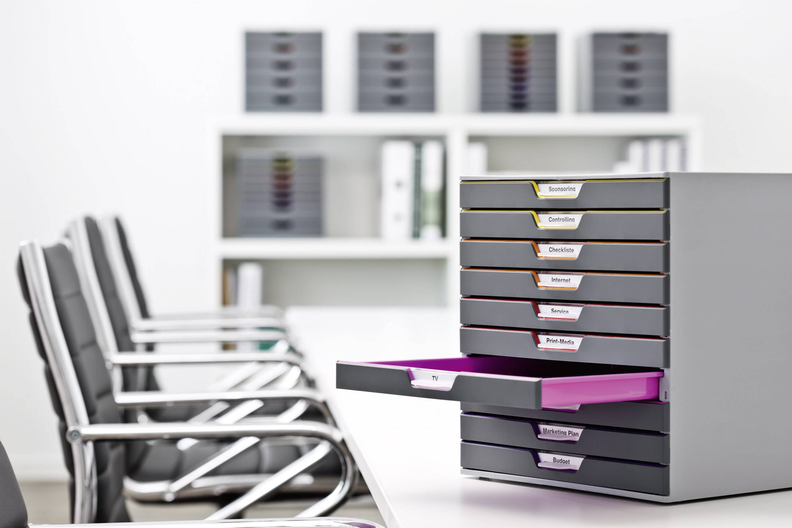 An office with a white desk, featuring a document holder with open drawers in various colours. Filing cabinets are visible in the background.
