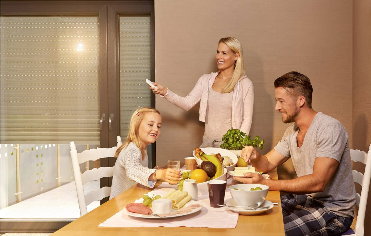 Family at the dining table: A man, a woman and a girl are happily having breakfast together. Fruit and bread are laid out on the table.