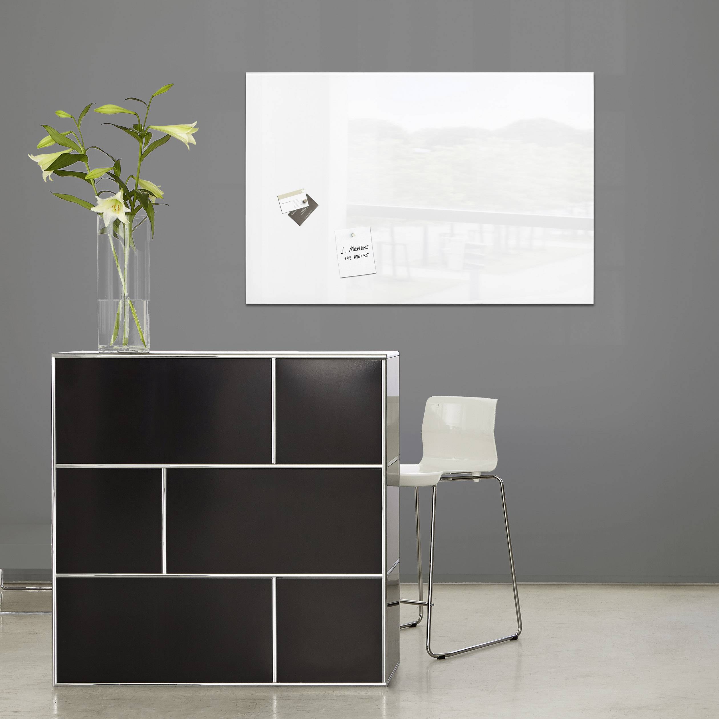 A modern, minimalist space with a black counter, featuring a vase of flowers atop it and a white chair to the side.
