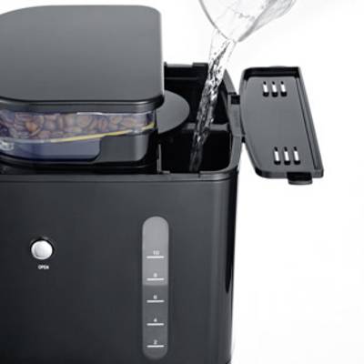 A coffee machine with a water reservoir is filled with a jug of water. At the top, there is a compartment containing coffee beans.