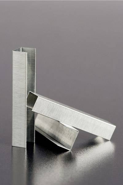 A stack of silver-coloured staples, some standing upright, on a smooth, grey surface.