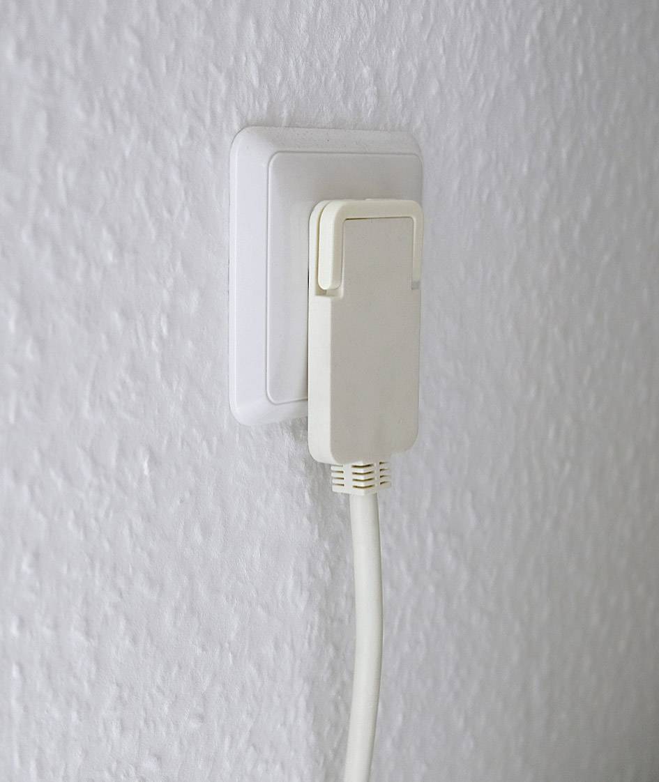 A white power cable is plugged into a white socket on a textured wall.