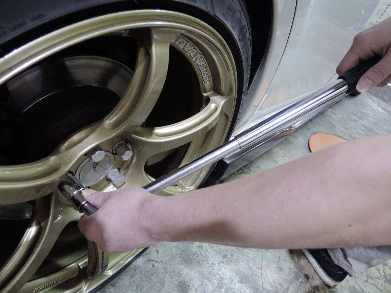 A person is tightening the wheel nuts of a golden car tyre using a torque wrench.