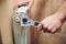 A person is tightening the valve head of a radiator against a beige tiled wall using an adjustable spanner.