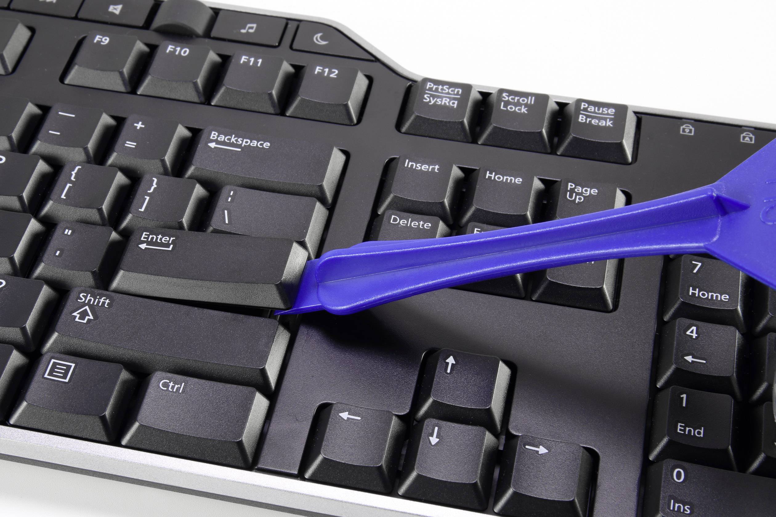 A black computer keyboard with a blue tool pointing at the Enter key to demonstrate its removal.