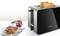 Black toaster with two golden-brown slices of toast. Beside it, a plate with toast spread with jam and a jar of jam.