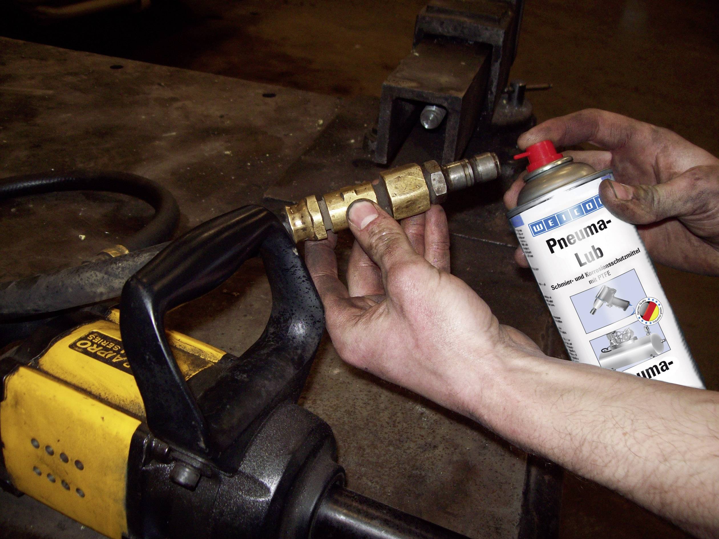 A person is holding a spray can of lubricant and spraying it onto a metal joint on a yellow power tool.