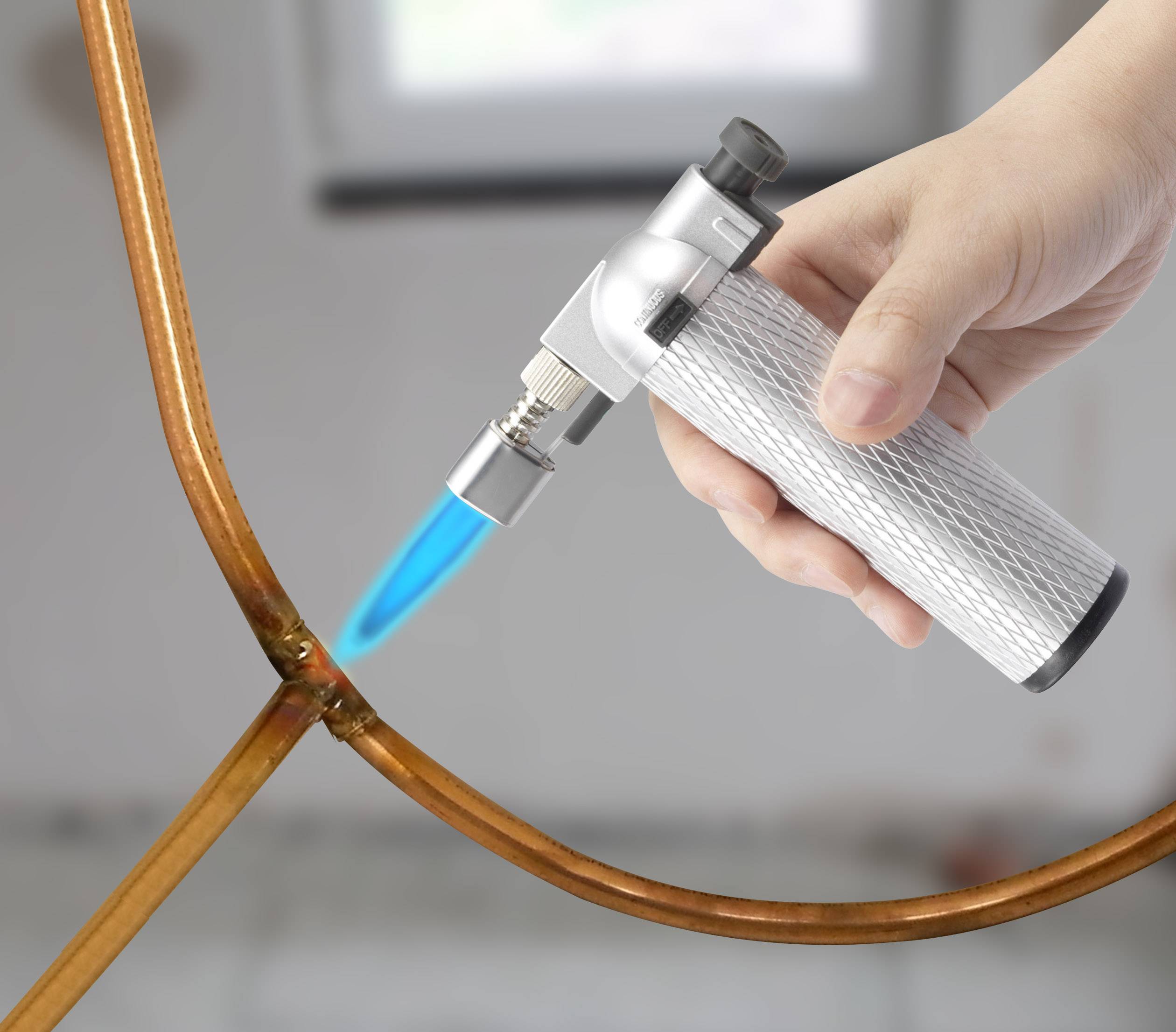 A hand is holding a small welding torch and heating a copper pipe, possibly in the context of repairs or installations.