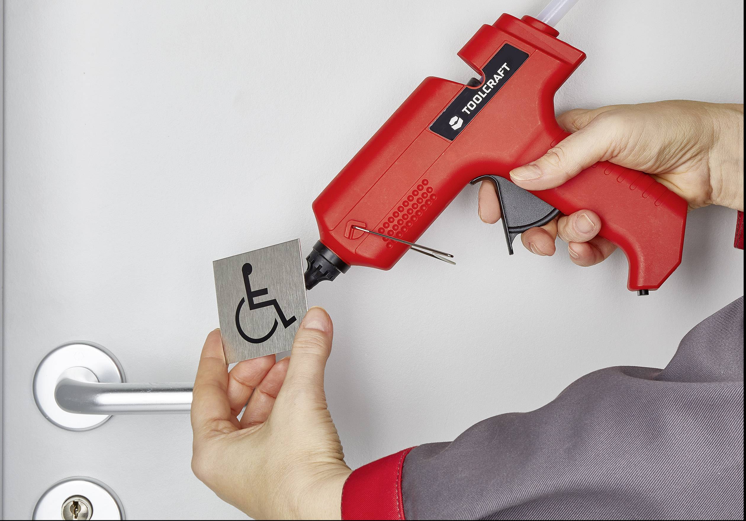 A person is holding a hot glue gun and attaching a sign with a wheelchair symbol to a door.