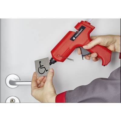 A person is holding a hot glue gun and attaching a sign with a wheelchair symbol to a door.