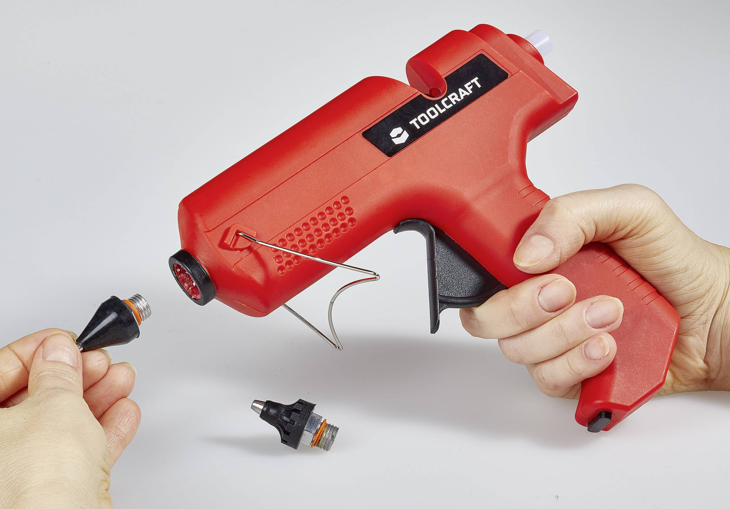 A hand is holding a red hot glue gun, while another hand is changing the nozzle.