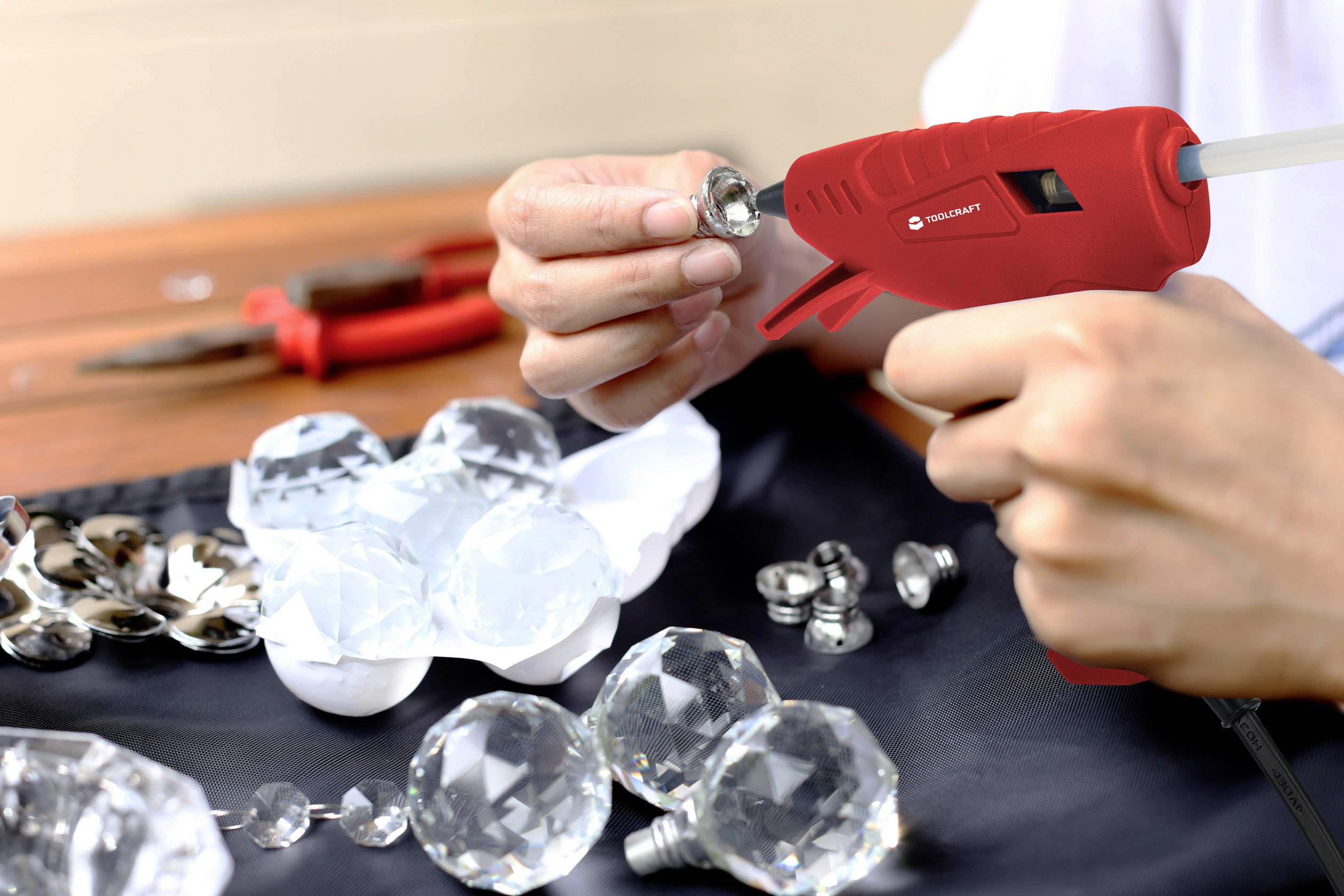 A person is using a hot glue gun to secure crystals. Tools are laid out in the background. Scene of a crafting activity.