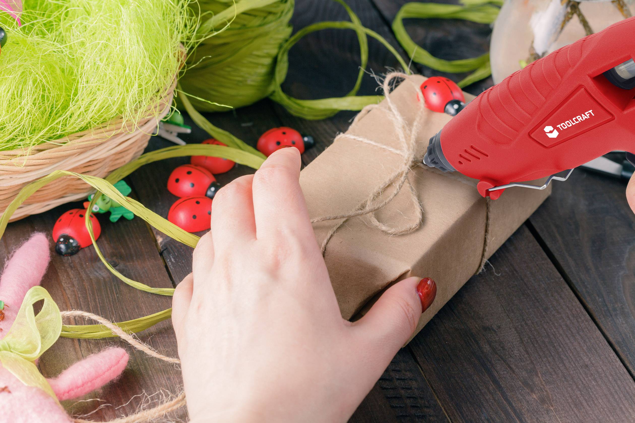 A person is using a hot glue gun to decorate a gift. There are spring decorations and colourful ribbons around it.