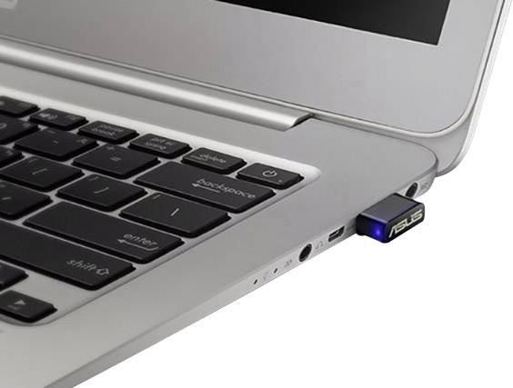A USB stick is plugged into a silver laptop. The laptop is switched on and displays a partially opened webpage.