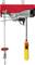 Electric winch with a red housing, steel cable, and yellow remote control. Used for lifting heavy loads in workshops.