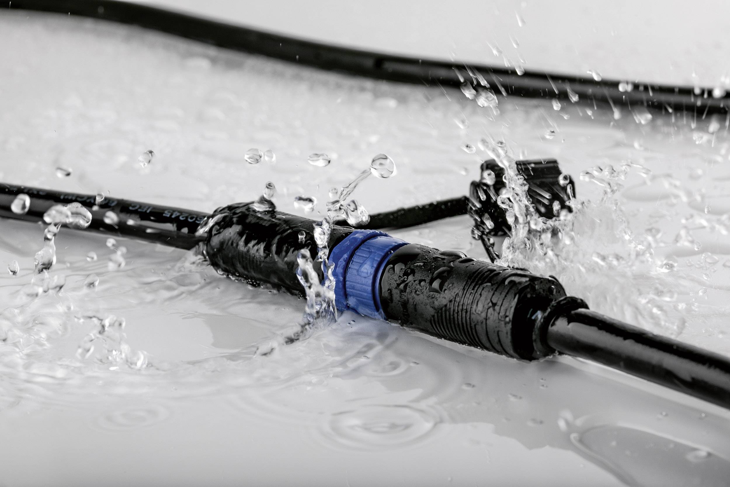 A waterproof cable connector, surrounded by splashing water, demonstrates the water resistance of the product in a wet environment.