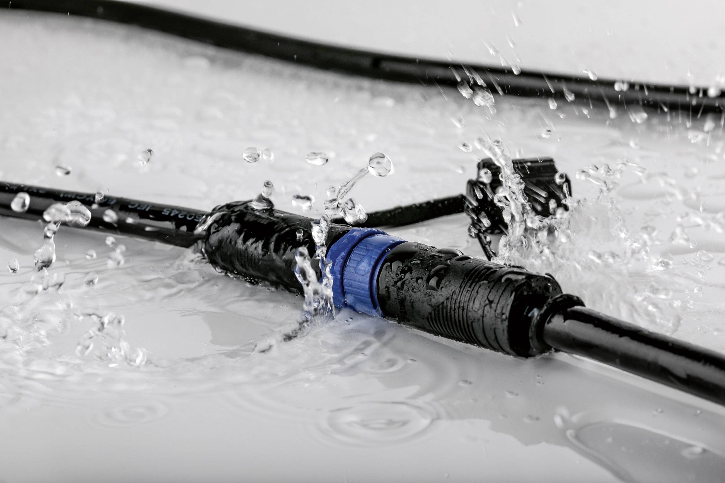 A waterproof cable connector in close-up, splash-proof and surrounded by water droplets, illustrates its robustness.