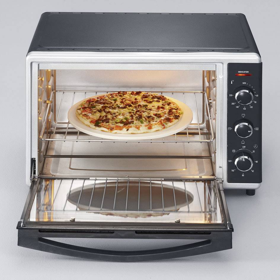 A small oven with an open door, with a pizza resting on the rack. The oven has several rotary knobs on its side.