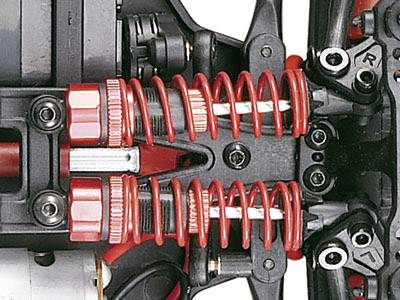 Close-up of a red, double suspension of an RC car, mounted on the front axle, revealing complex mechanical components.