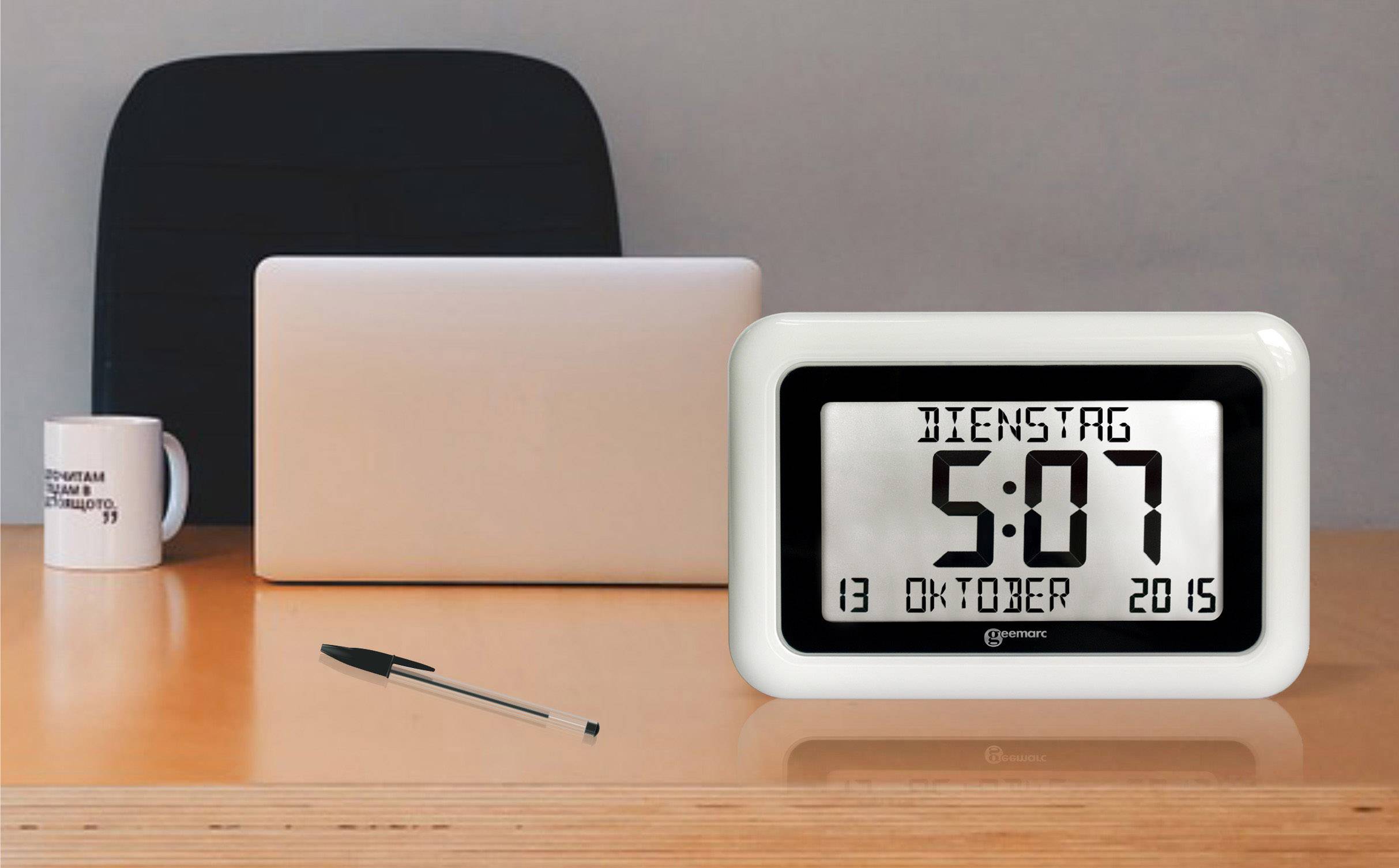 A digital clock displays 'TUESDAY 5:07'. Date is '13 OCTOBER 2015'. In the background, a desk with a laptop, mug and pen.