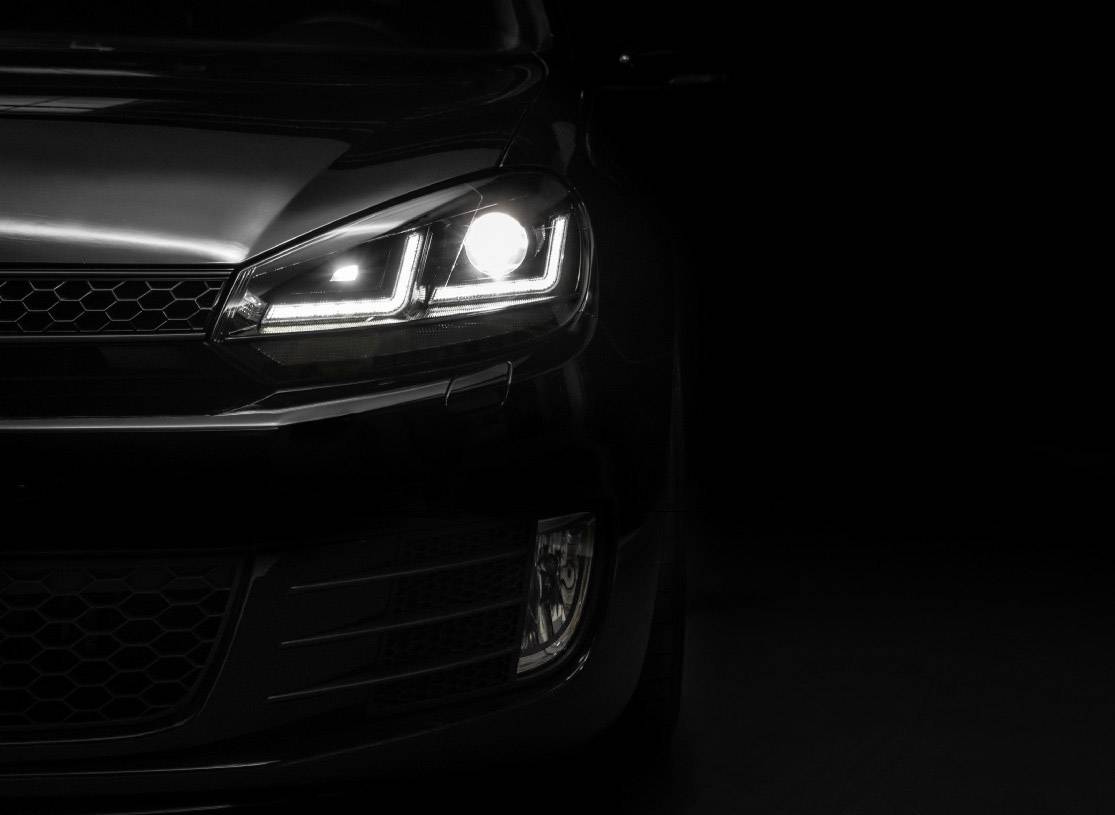 The front of a car with its headlight switched on is visible in the darkness. The front displays modern, clean lines.
