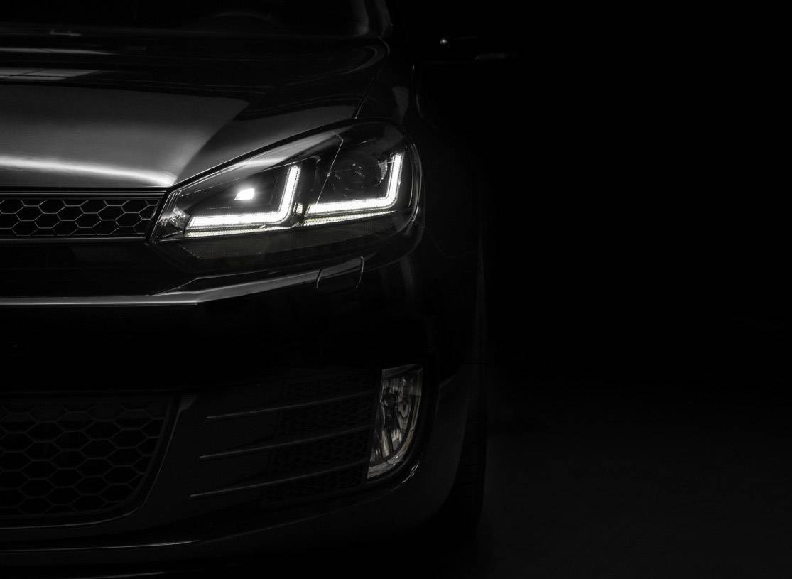 The headlight of a black car illuminates in a dark room, focused on detail and design.