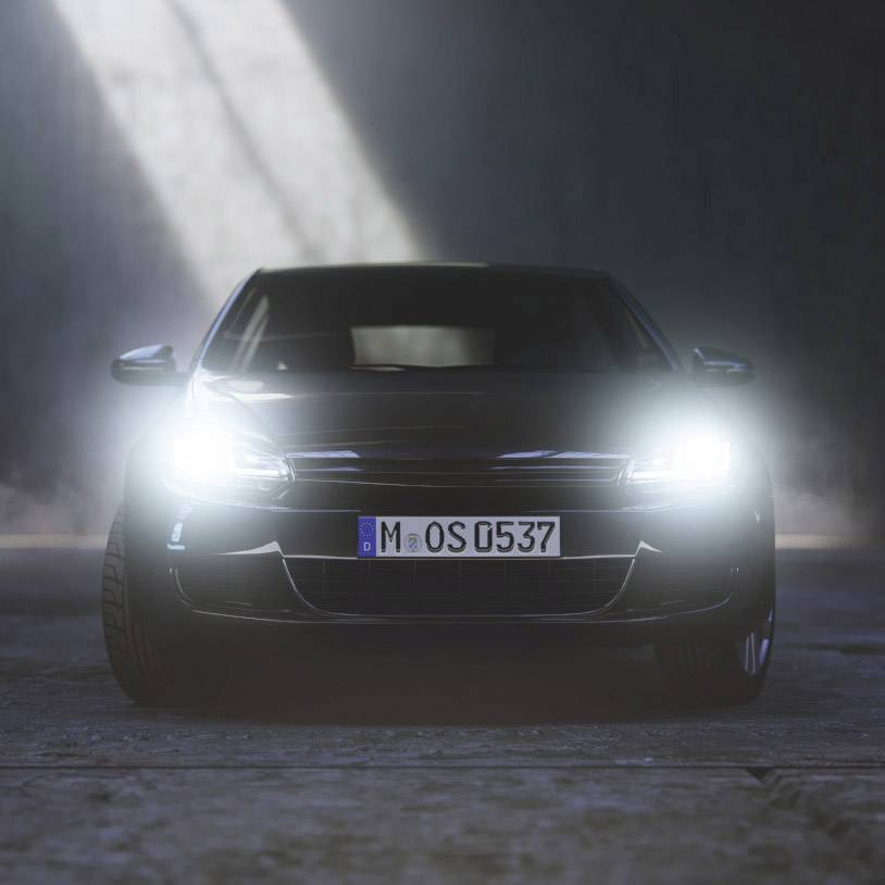 A car with its headlights on is parked at night in a dark room, viewed from the front.