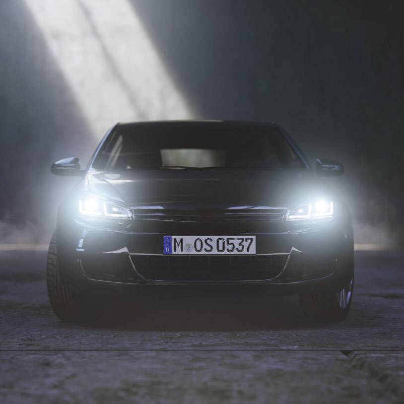 A modern car with headlights on, seen frontally in a dark environment.