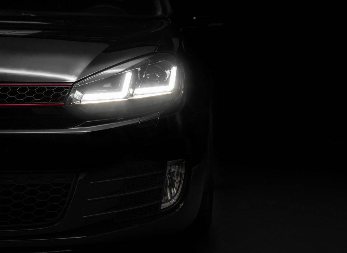 A car in the dark shows its glowing headlights. Only the front section is visible, creating a strong contrast.