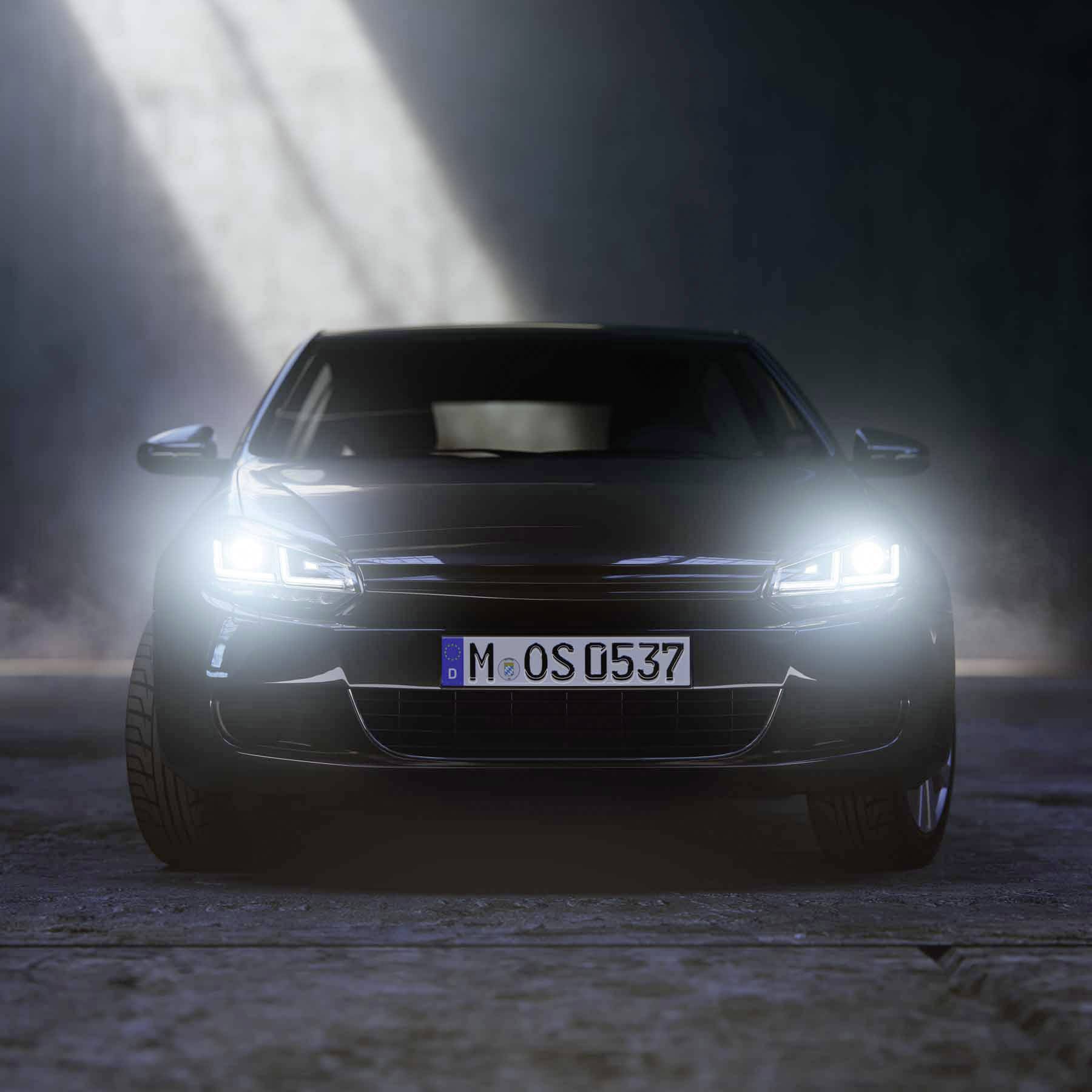 A black car with its headlights on is parked in a dark environment, photographed from the front.