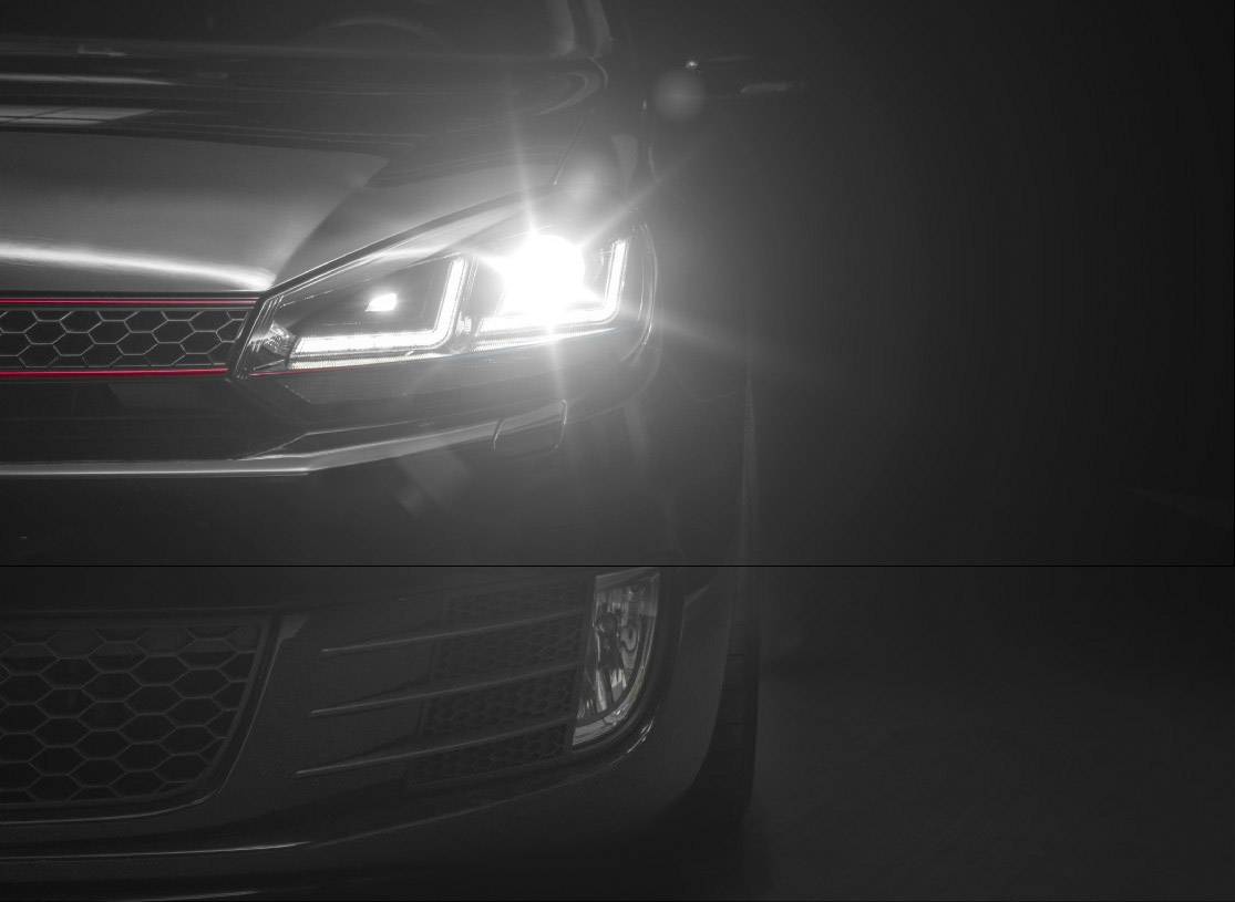 Car at night, headlights on, illuminating the road. Front view focused on the right light.