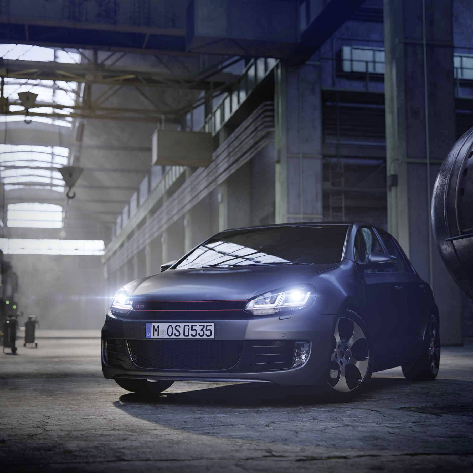 A dark blue compact car is parked in a large, industrial-looking hall with high windows and streaming light.