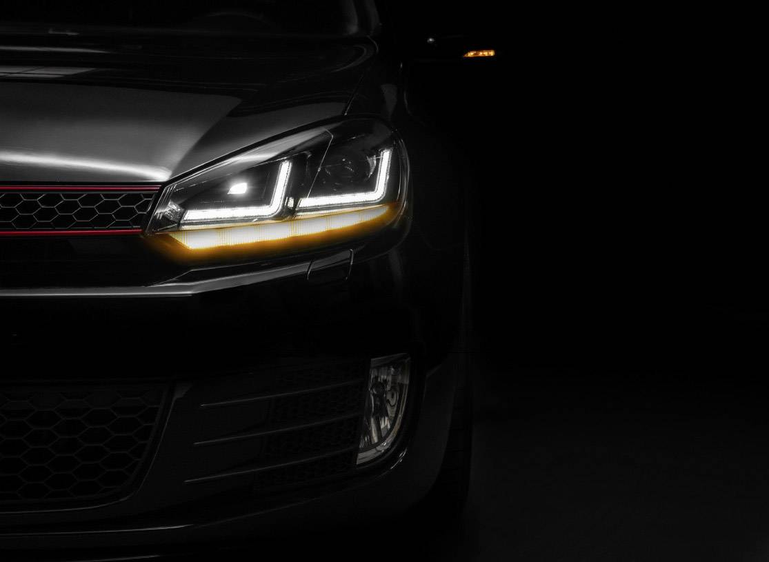 Close-up of a car headlight in a dark room. The lights are switched on and shine brightly into the darkness.