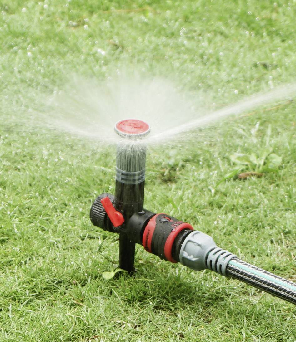 A garden sprinkler is watering a green lawn evenly. It rotates to distribute water in a circular pattern.