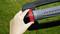 A hand turns a red button on a garden device against a green lawn background.