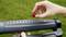 A person inserts a red dropper into a grey garden irrigation hose. Background of blurred green grass.