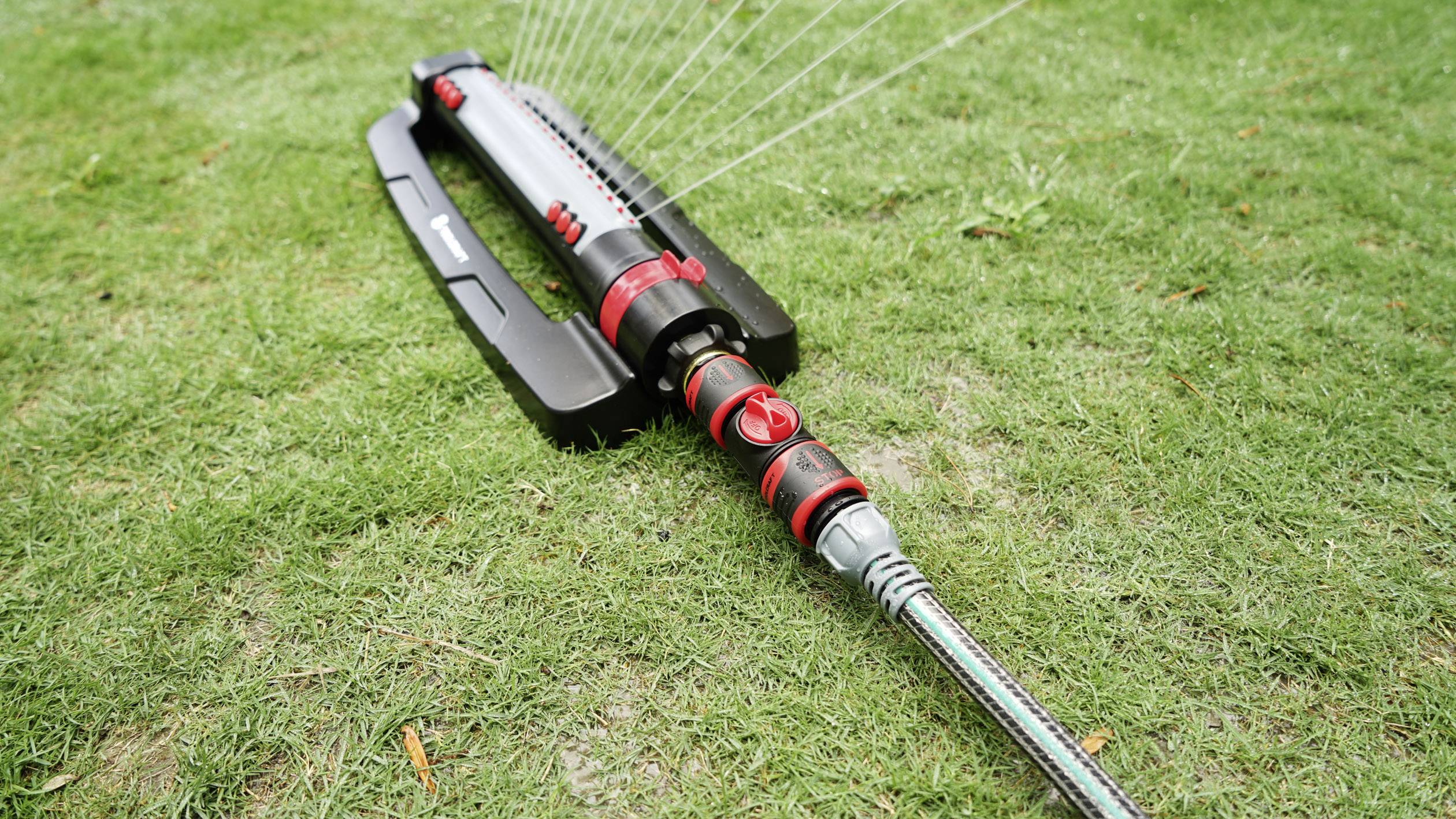 Lawn sprinklers on a meadow spray water in an even pattern to irrigate the grass.