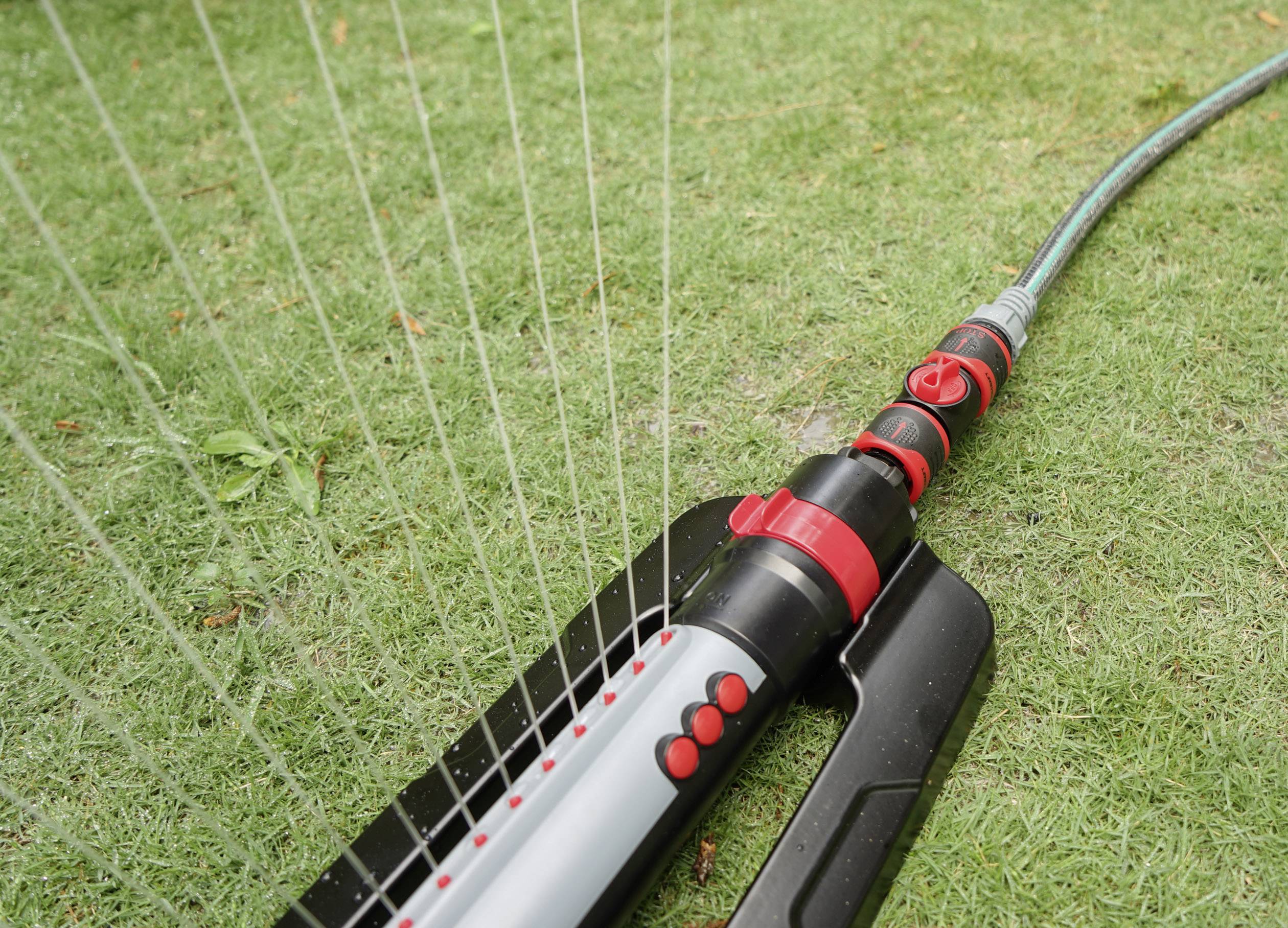 A lawn is being watered with an oscillating garden sprinkler. The sprinkler is spraying water in multiple lines across the grassy area.