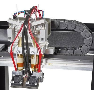 Close-up of a 3D printer extruder unit with wiring, tubes, and fans mounted on a rail.